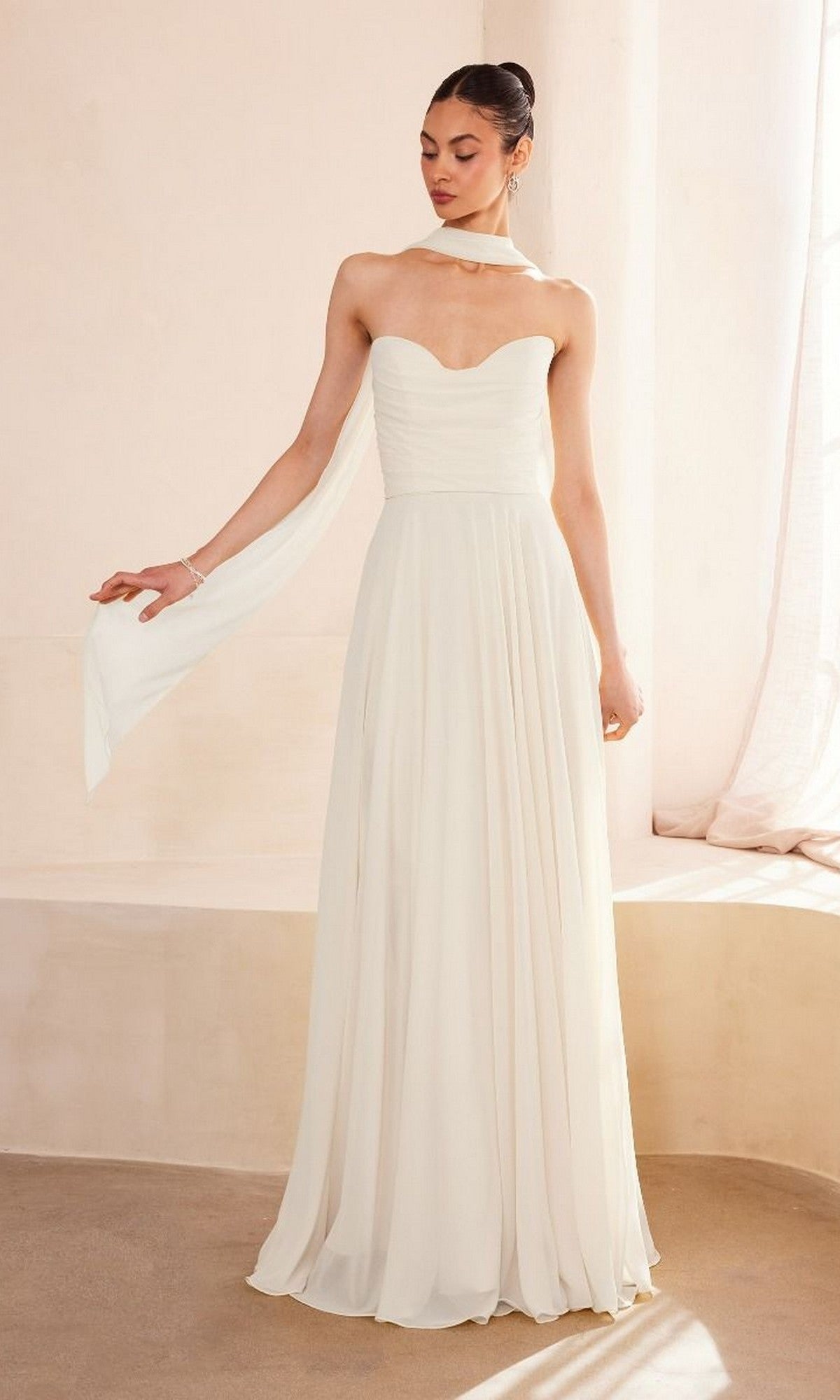 A woman wearing the affordable Amoris T703W Strapless Long White Wedding Dress—with a sweetheart neckline and matching scarf—stands indoors.